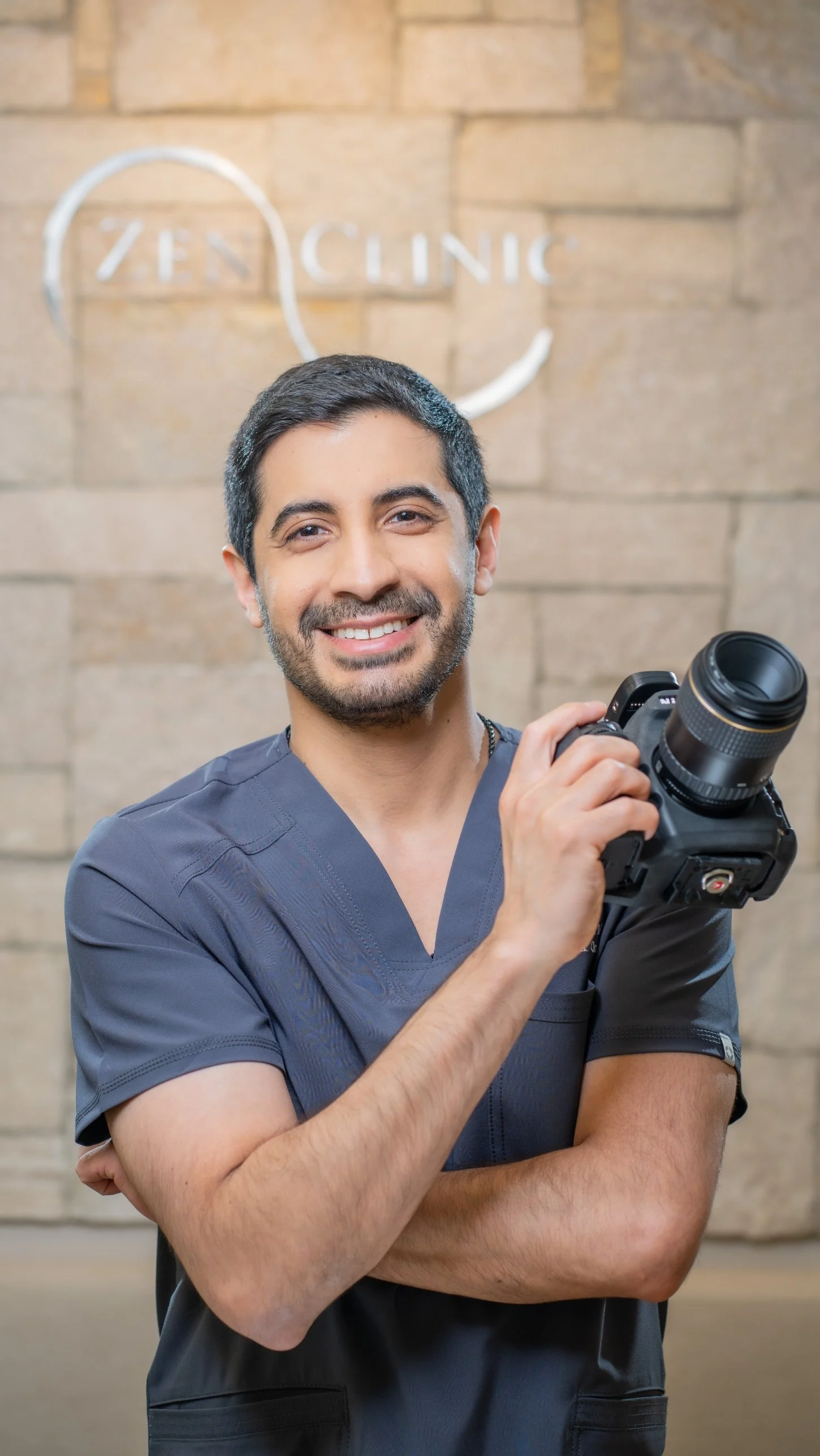 El Dr. Ravi Khubani Mirvani con su cámara fotográfica frente al logo de Zenclinic Dental; la fotografía clínica es parte de su protocolo de carillas